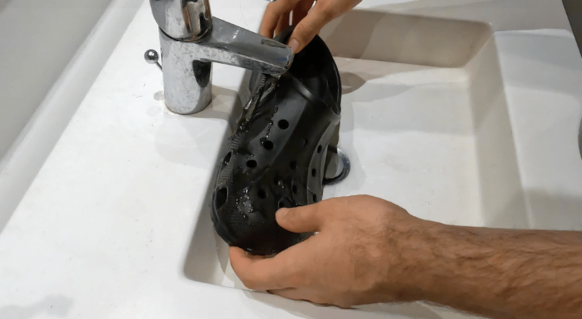 Black regular croslite clog being rinsed under tap water
