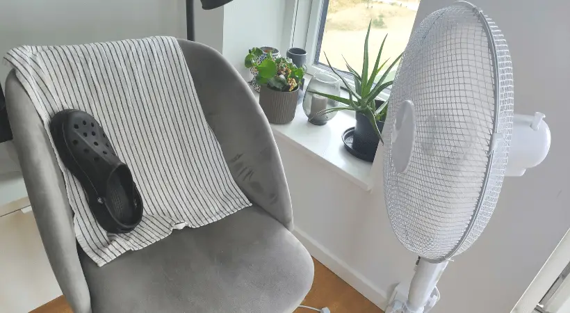 A single crocs clog is placed vertically on a chair in front of an electric fan.