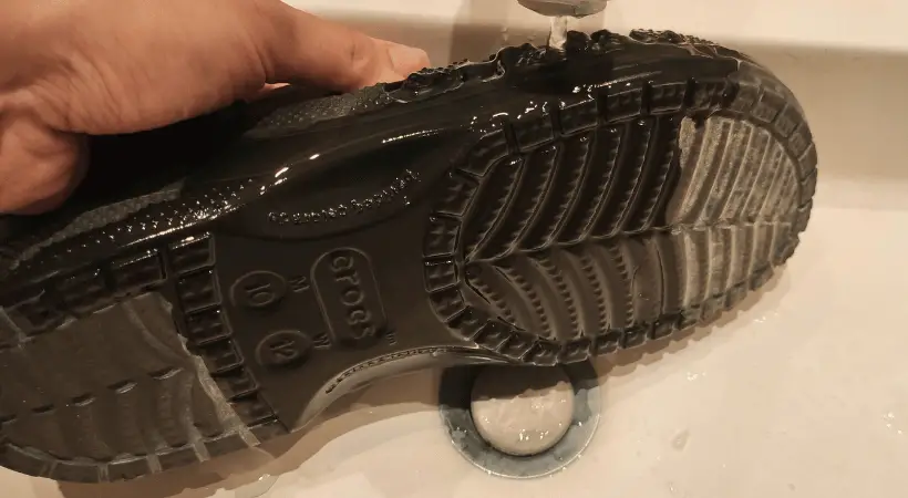 Dirty black Crocs being washed under running tap water